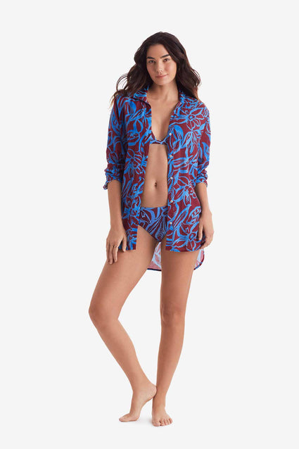 Woman wearing a button down long sleeve shirt with blue and brown abstract floral print unbuttoned