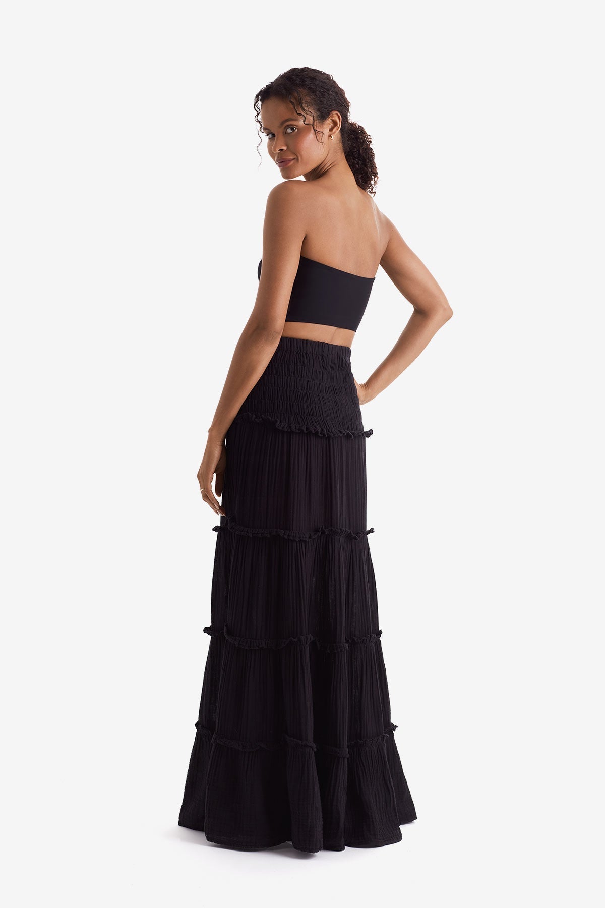 Woman turned left wearing a black bandeau top and black floor length skirt