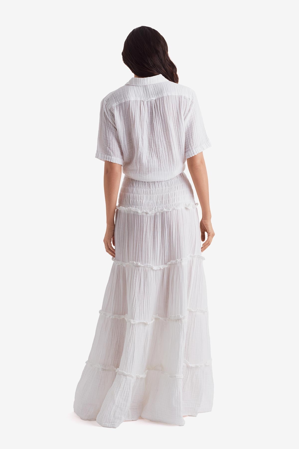 Woman faced away wearing a white short sleeve button up and white floor length skirt