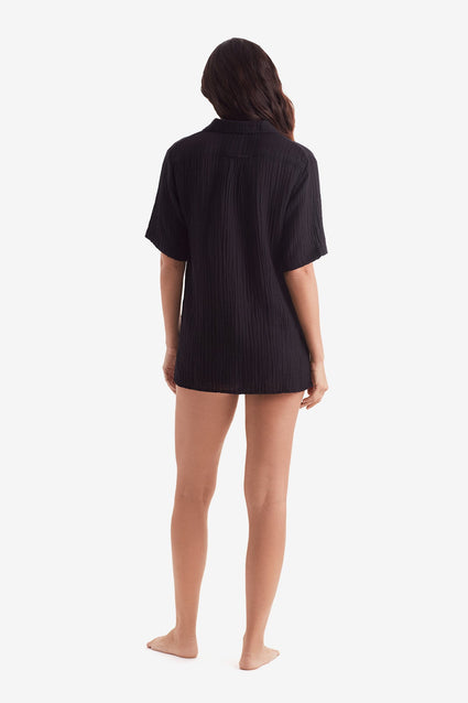 Woman faced away wearing a black short sleeve button up shirt