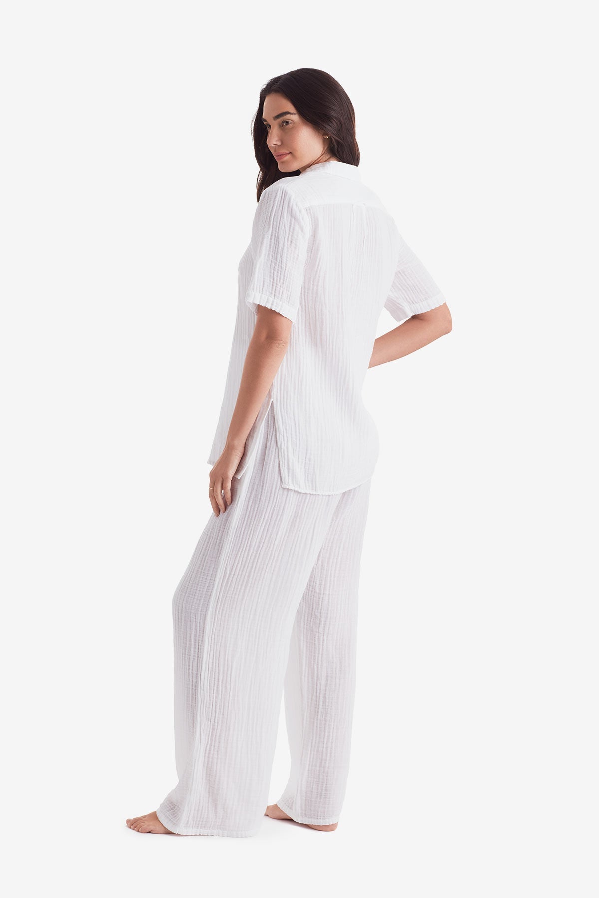 Woman turned left wearing a white short sleeve button up and white beach pants