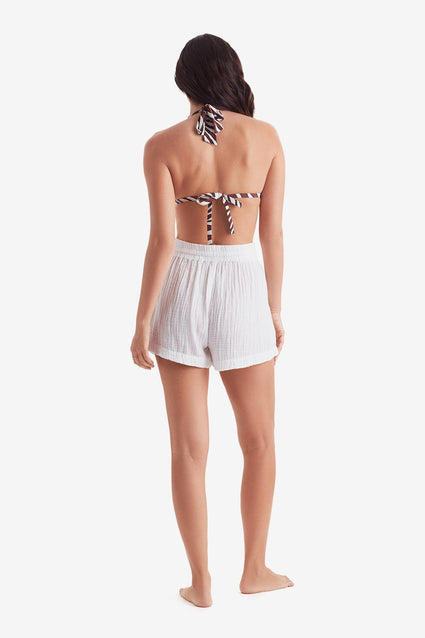 Woman faced away wearing a zebra print bikini top with white beach shorts