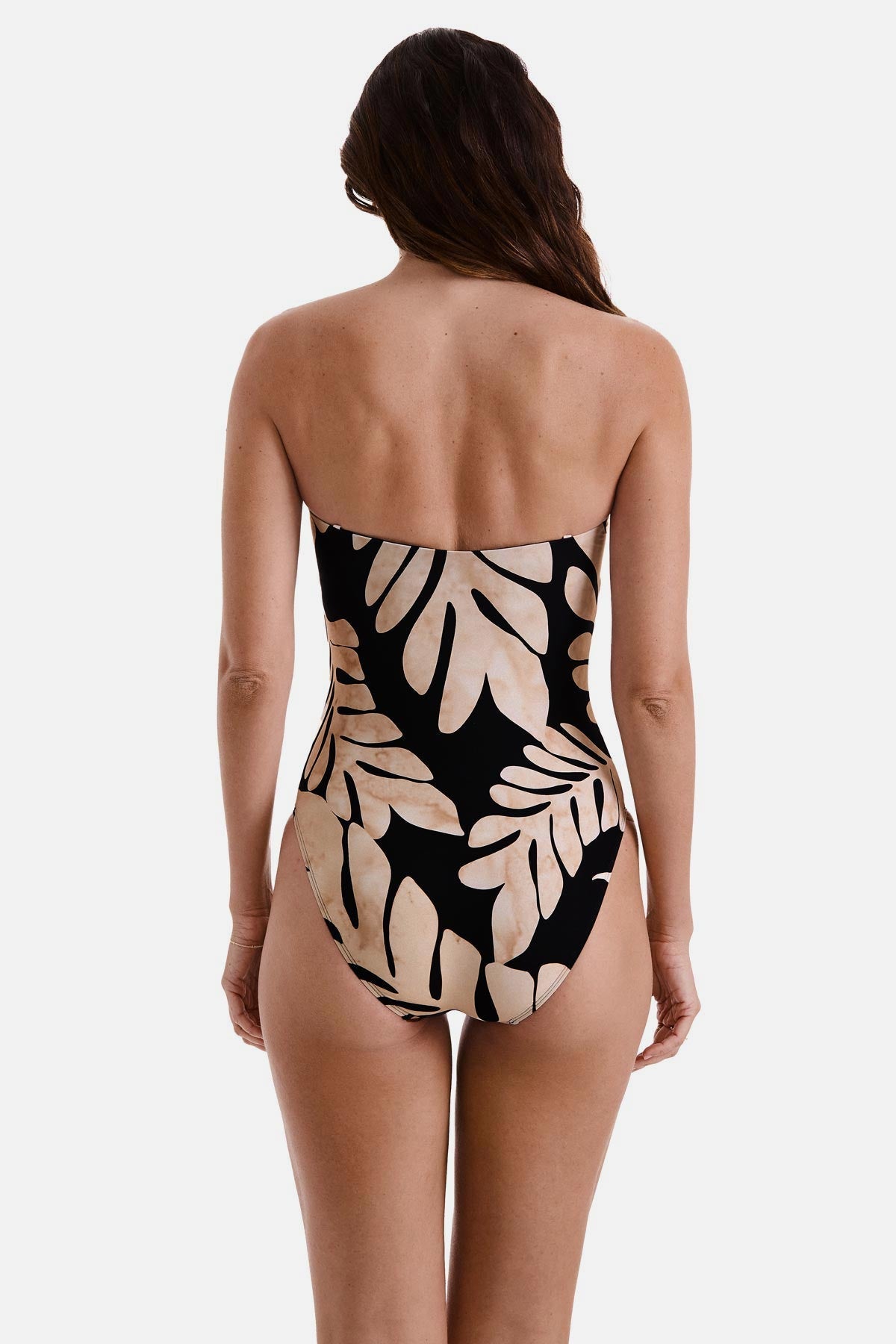 Woman turned away wearing a bandeau one-piece swimsuit with a black and tan palm leaf print
