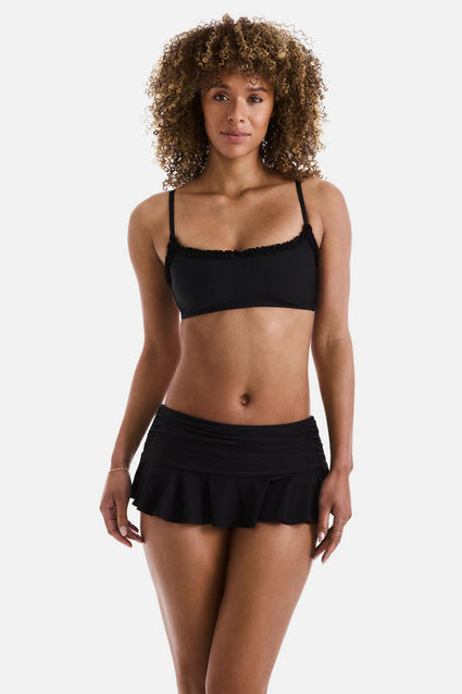 Woman wearing a black bralette swim top with black skirted swim bottoms