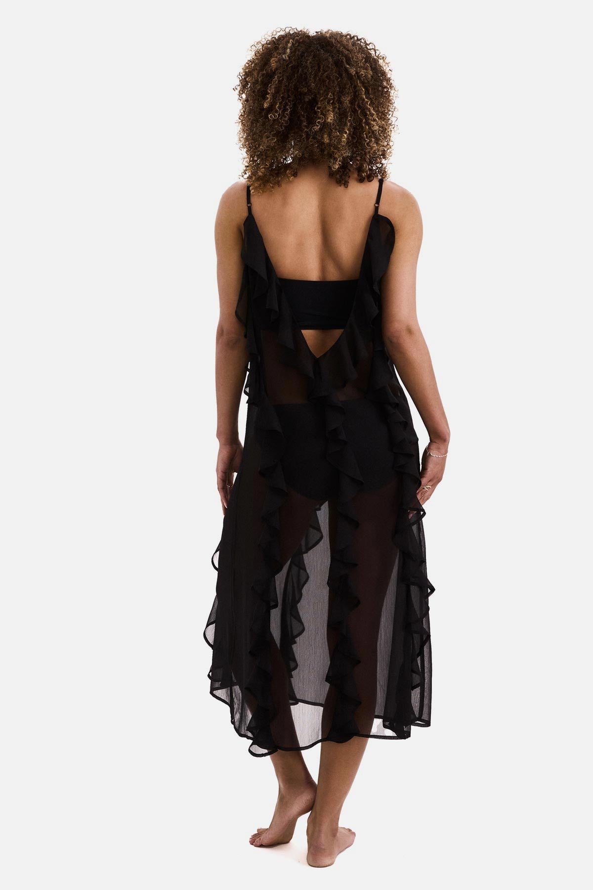 Woman turned away wearing a black sheer ruffled swim dress cover up