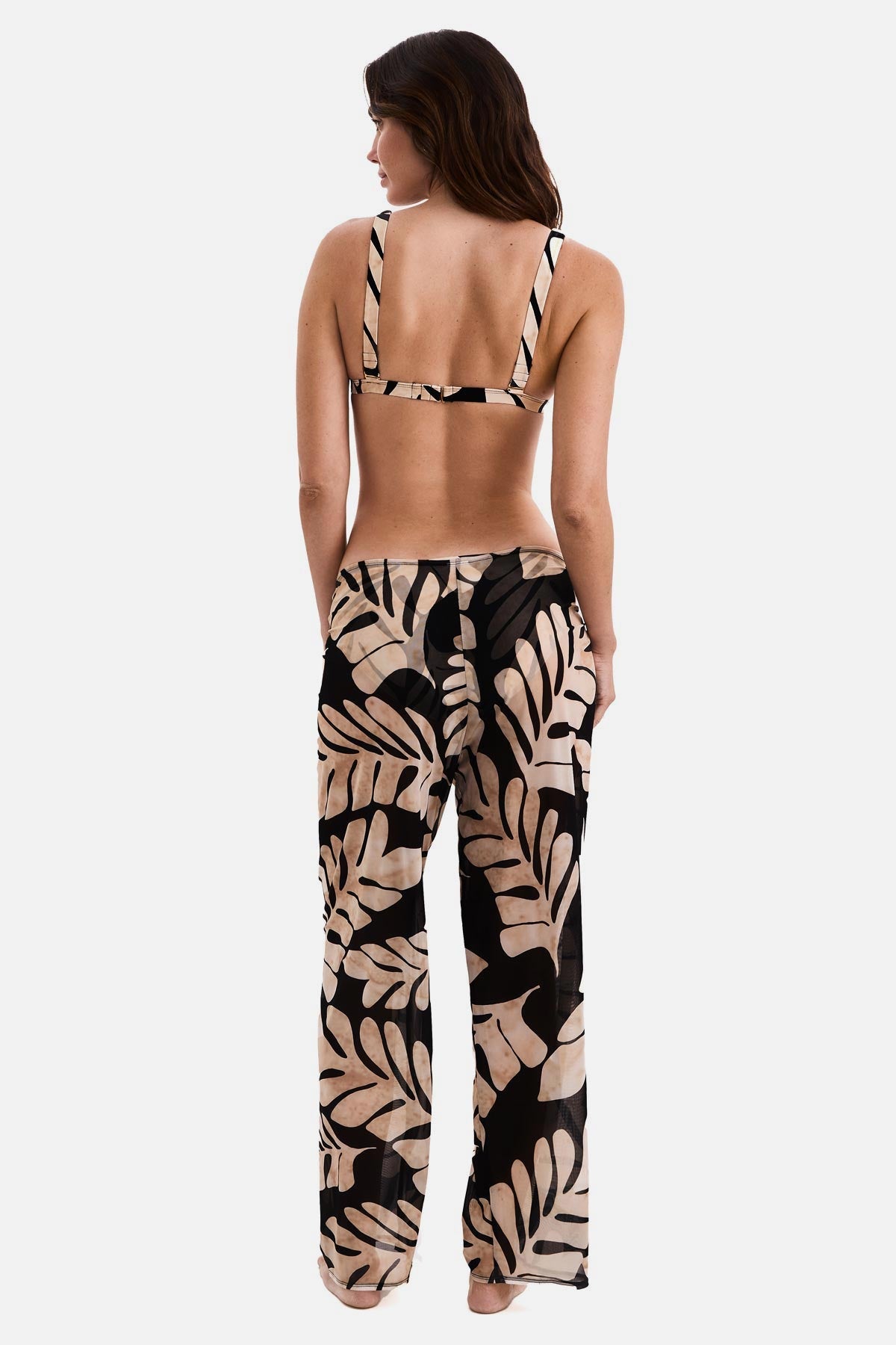 Woman turned away wearing black and tan palm leaf printed swim cover up pants with a matching bikini top