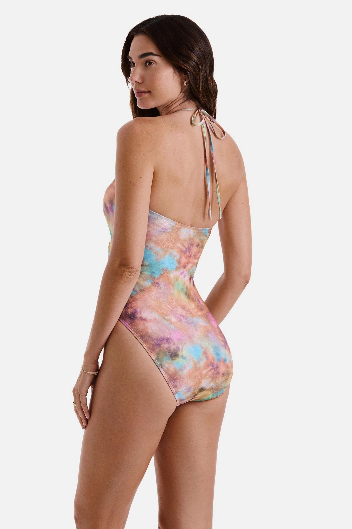 Woman turned left wearing a tie dye one-piece swimsuit with a halter tie
