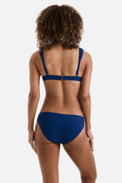 Woman turned away wearing a dark blue bikini top with matching swim bottoms