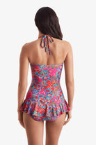 Woman turned away wearing a multicolored bandeau and skirted leg one-piece swimsuit