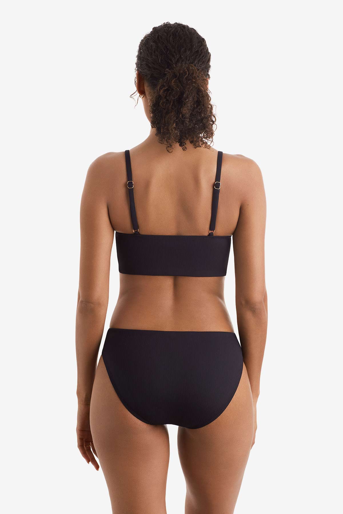 Woman faced away wearing a black midkini swim top with black swim bottoms