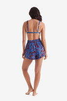 Woman faced away wearing an abstract floral print bikini top with abstract floral print beach shorts