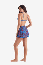 Woman faced left wearing an abstract floral print bikini top with abstract floral print beach shorts
