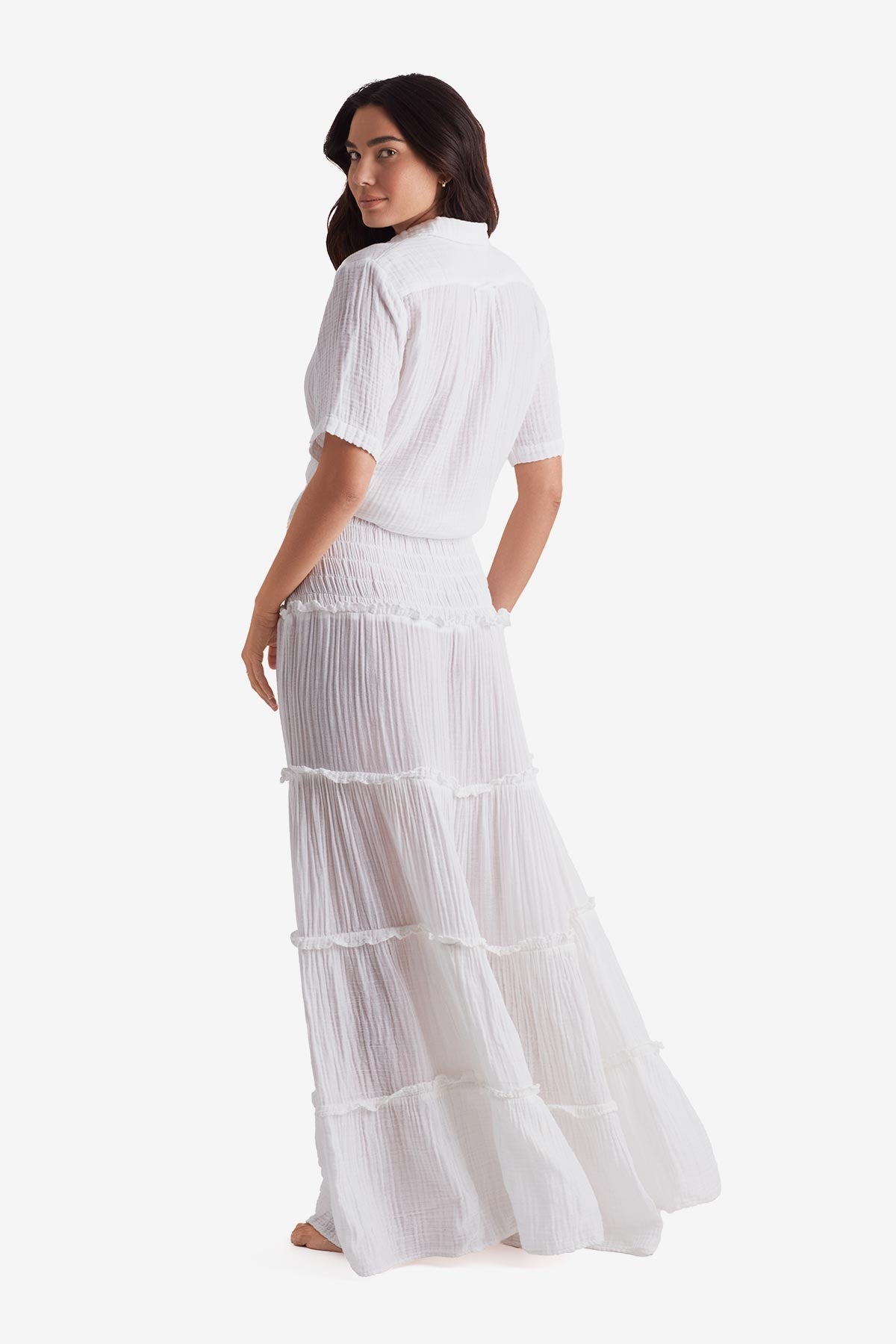 Woman faced left wearing a white short sleeve button up and white floor length skirt