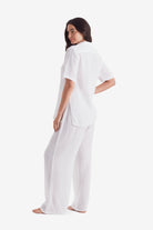 Woman turned left wearing a white short sleeve button up and white beach pants
