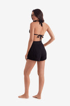 Woman turned left wearing a black bikini top and black shorts