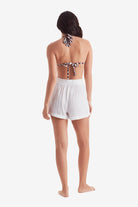 Woman faced away wearing a zebra print bikini top with white beach shorts