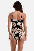Woman turned away wearing a large tan and black leaf printed tankini top with matching swim bottoms