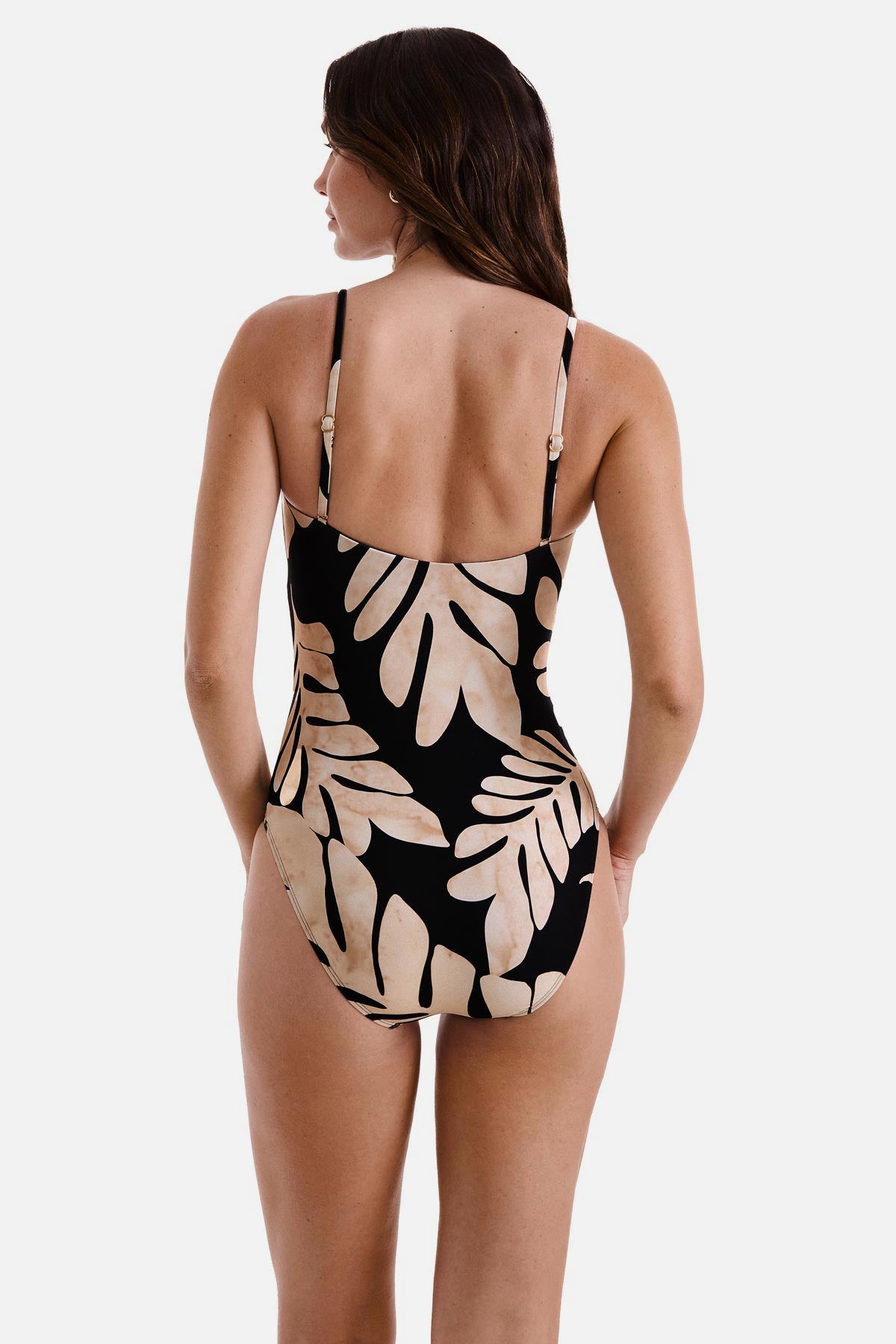 Woman turned away wearing a one-piece swimsuit with a black and tan palm leaf print 