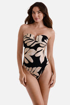 Woman wearing a one-piece bandeau swimsuit with a black and tan palm leaf print 
