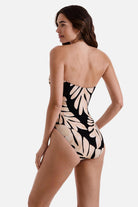 Woman turned left wearing a one-piece swimsuit with a black and tan palm leaf print 