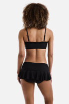 Woman turned away wearing a black bralette swim top with black skirted swim bottoms