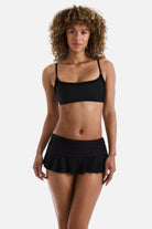 Woman wearing a black bralette swim top with black skirted swim bottoms