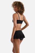 Woman turned left wearing a black bralette swim top with black skirted swim bottoms