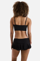 Woman turned away wearing a black midkini tankini swim top with matching skirted swim bottoms