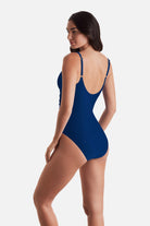 Woman turned left wearing a dark blue one-piece swimsuit with ruffles on the edges