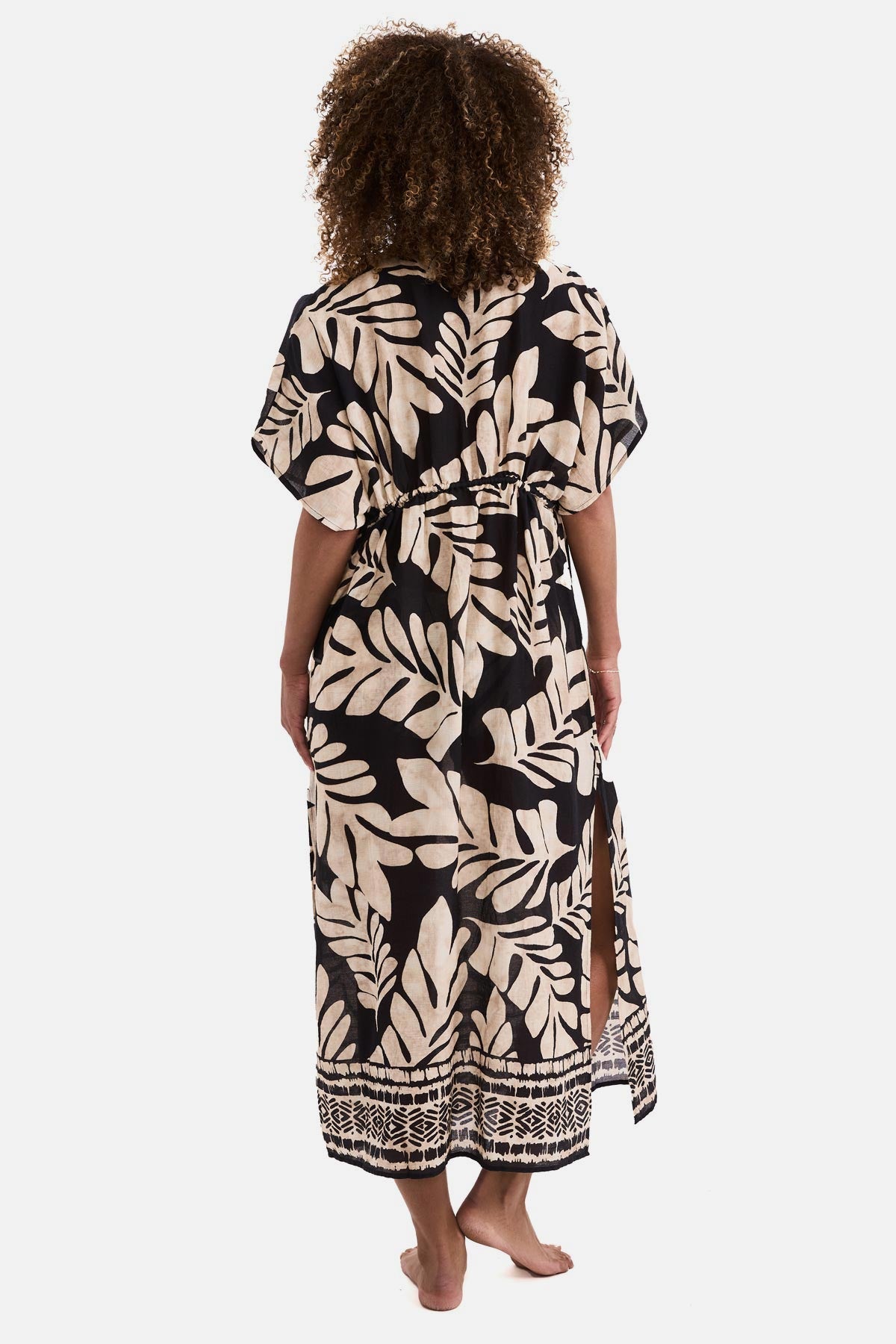 Woman turned away wearing a black and tan palm leaf printed swim dress cover up