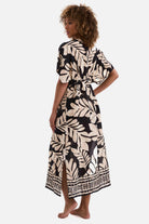 Woman turned left wearing a black and tan palm leaf printed swim dress cover up