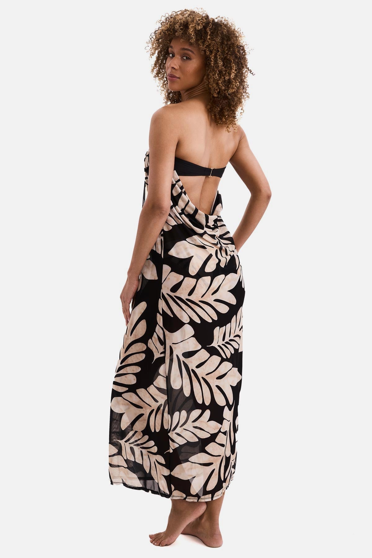 Woman turned left wearing a black and tan palm leaf printed sleeveless swim dress cover up