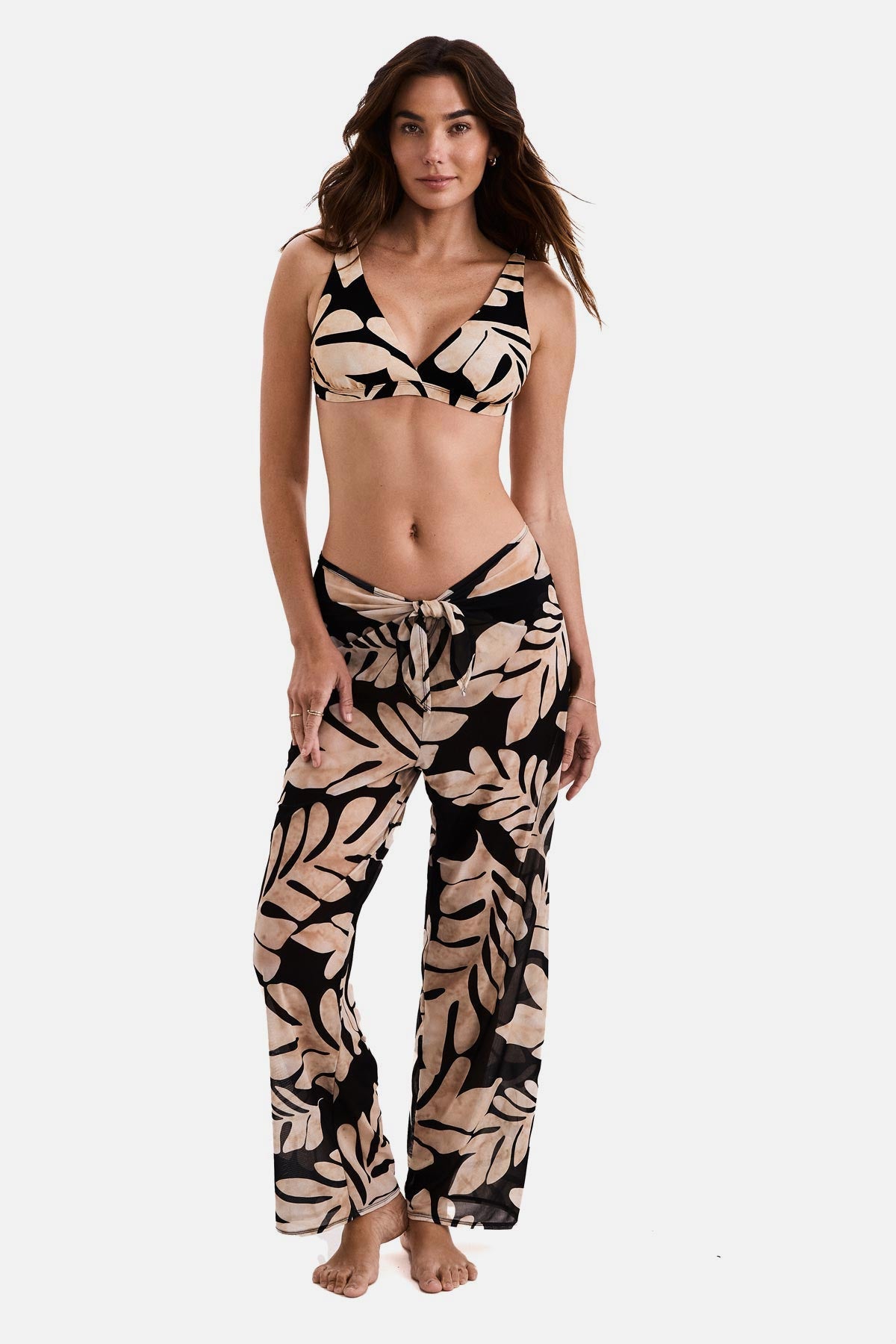 Woman wearing black and tan palm leaf printed swim cover up pants with a matching bikini top